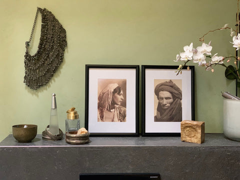 Zwei Portraitbilder in alten Rahmen auf einer Anrichte vor einer grünen Wand.