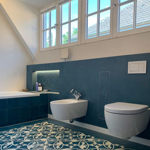 Stilvolles Badezimmer mit halbhohem, fugenlosem Wandbelag in tiefem Blau, kombiniert mit floralen Bodenfliesen – moderne Badgestaltung mit mineralischer Oberfläche und mediterranem Flair