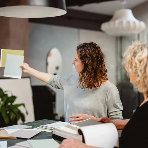 Die Malermeister Fee und Ursel Kohlmann betrachten zwei Farbmuster in ocker und mintgrün.