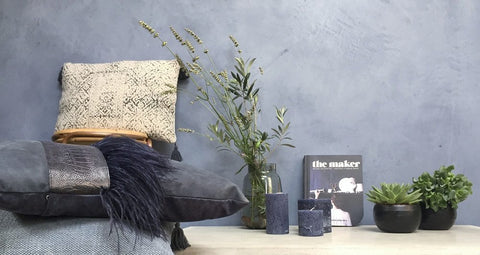 Eine mit Indigo Blau Naturfarbe angemalte Wand vor der Pflanzen und Kerzen stehen.