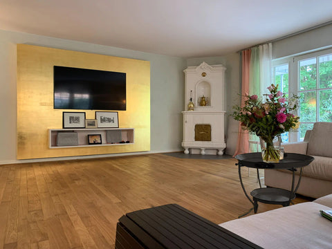 Modernes Wohnzimmer mit einer goldenen Wand, vor der ein großer LED-Fernseher steht.