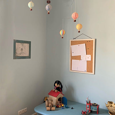 Ein mit hellblauer Naturfarbe gestrichenes Kinderzimmer, im dem Holzspielzeug steht und ein Mobile mit Papier-Fesselballons von der der Zimmerdecke hängt.